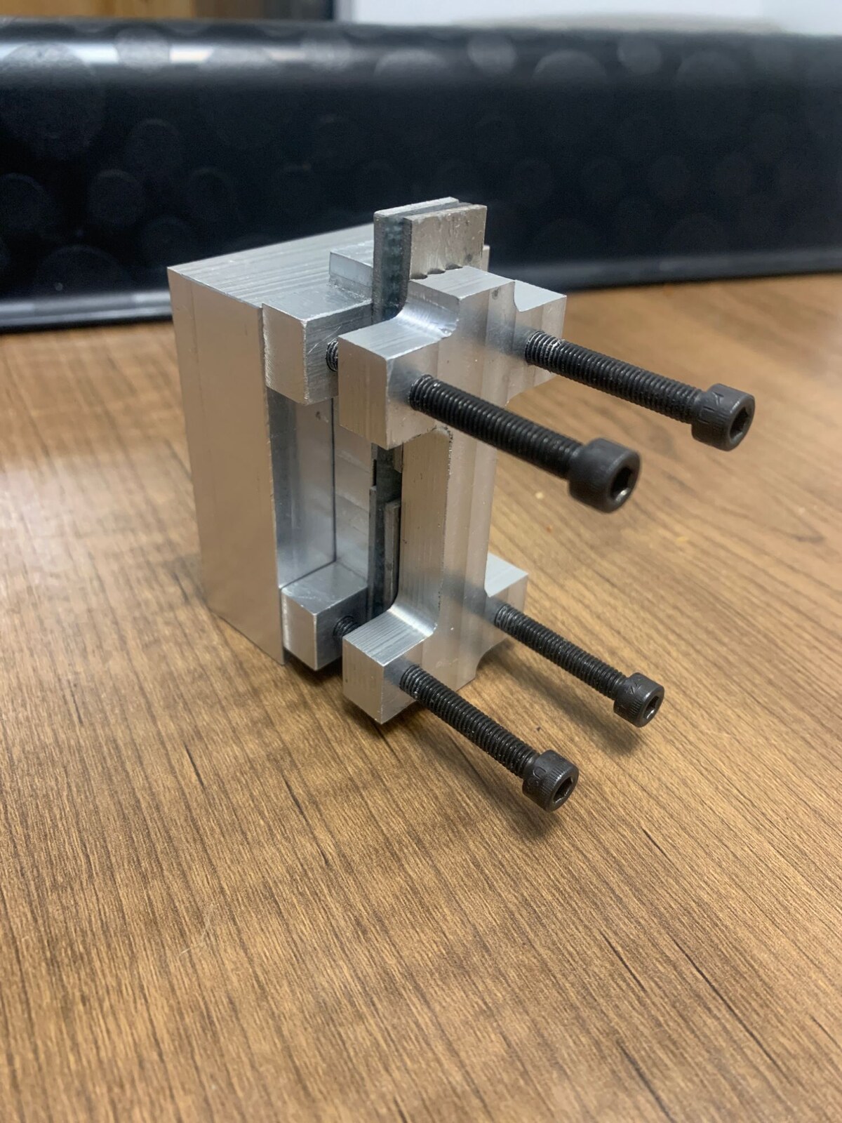 The machined aluminum compression-testing fixture with four socket-head cap screws, holding a coupon